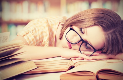 tired student girl with glasses sleeping on the books in the library